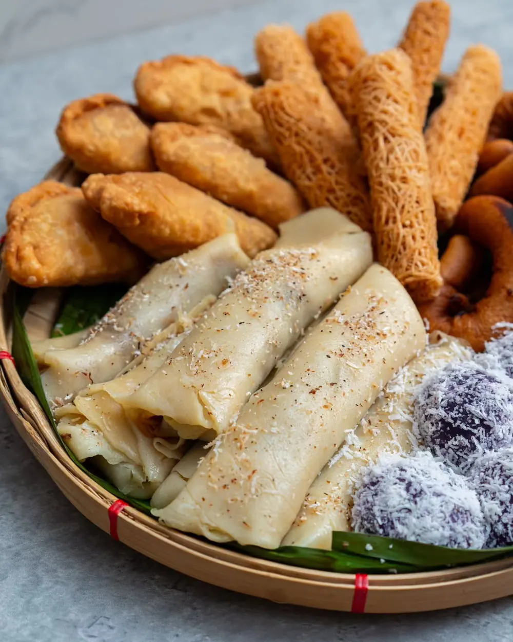 A woven tray of Tausug native cakes: rolled pancakes, sesame crackers, purple rice balls and fried rings.