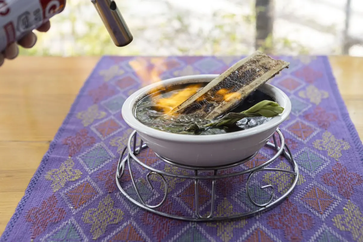 Tiyula Itum with a torched bone marrow, served on a stand over a purple woven cloth.