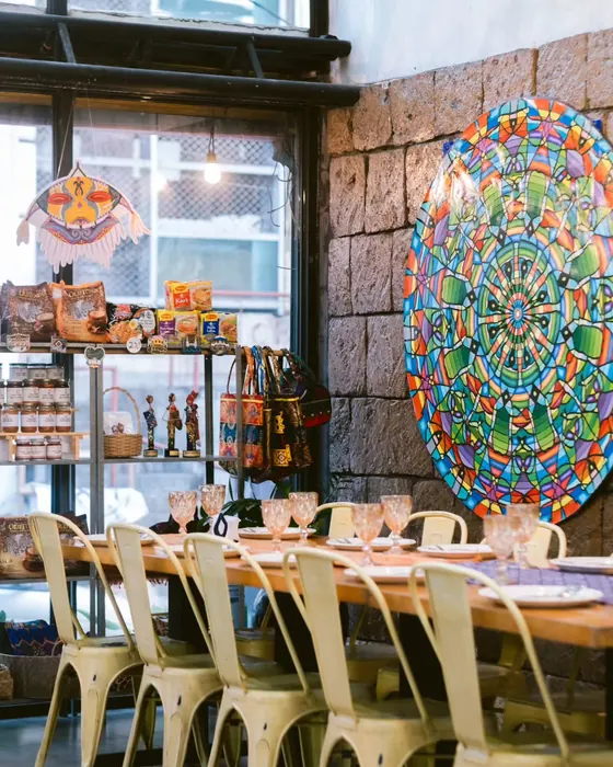 A long table set beside a stone wall hung with a large circular woven artwork.