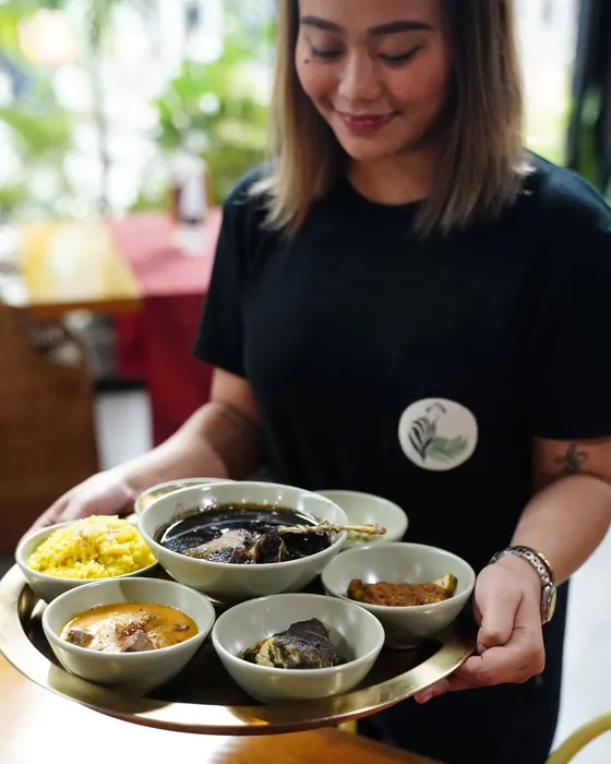 A server carrying a Dulang tray of small bowls.