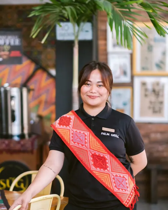 A smiling Palm Grill server wearing a red woven sash.