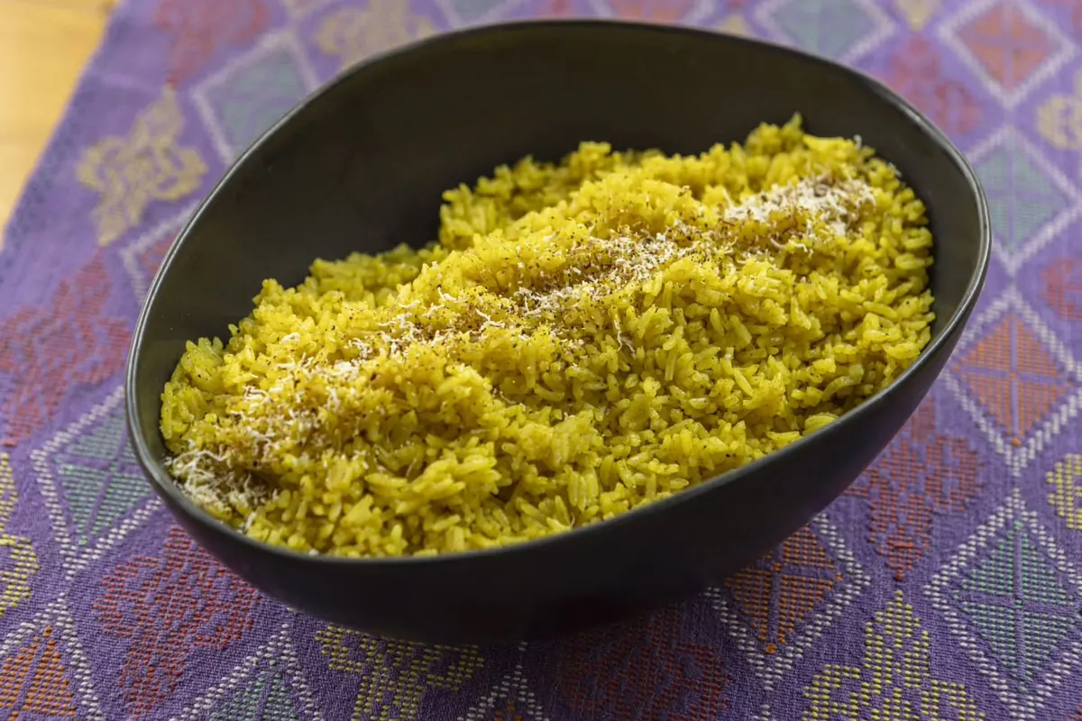 A black bowl of yellow turmeric rice on a purple woven cloth.
